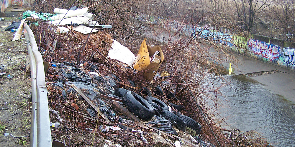 Trash and tires dumped over an urban river bank