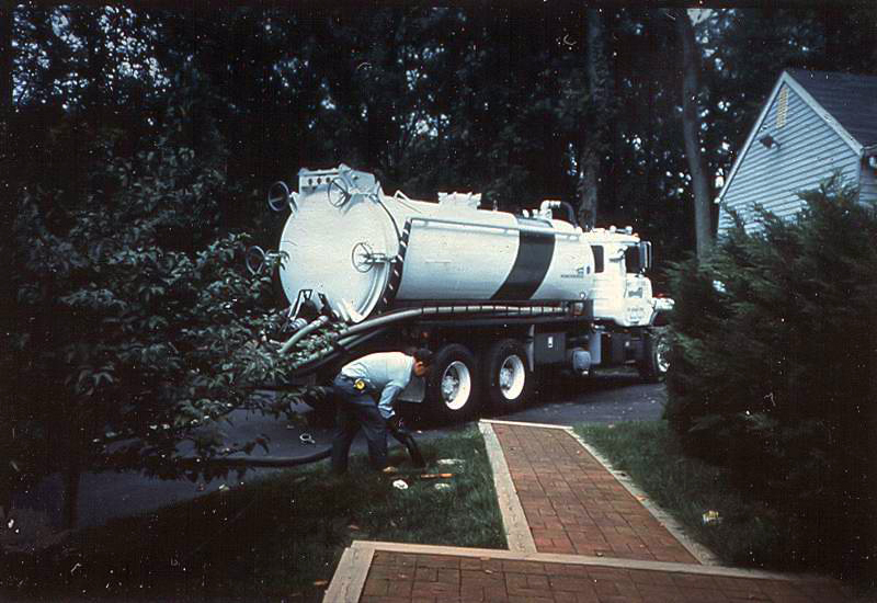 A white truck pumps out a septic system in front of a residence.