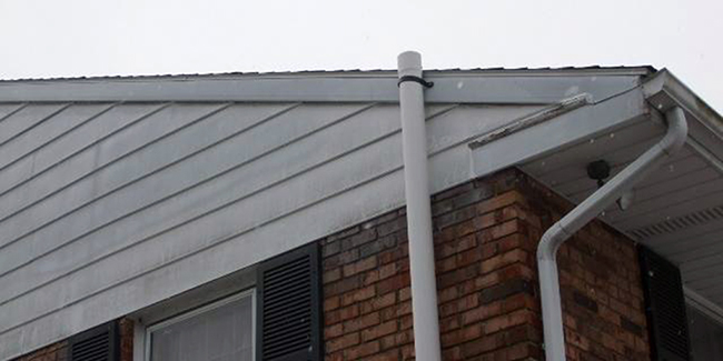 A radon mitigation pipe clears the roof line of a house