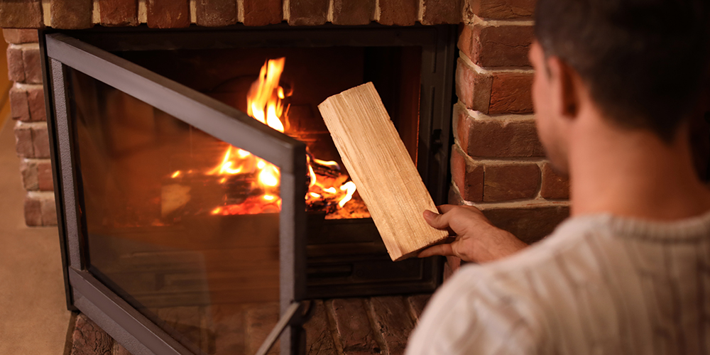 Man putting dry firewood into fireplace at home